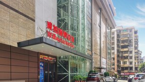 A modern building with a large glass facade, a prominent red sign, and a tiled entrance area.
