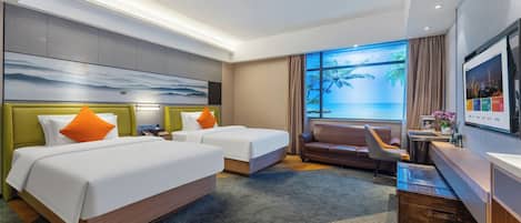 A hotel room with two beds, a sofa, a desk, and a large window with a view of the sea.
