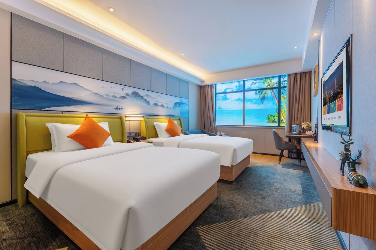 Quarto de hotel com duas camas, uma mesa, uma cadeira, uma janela grande com vista e um quadro na parede.