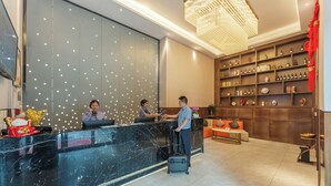 A hotel reception area with a marble counter, a chandelier, and a wall with shelves of bottles.