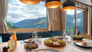Une table à manger avec un croissant, du fromage, des raisins et une bouteille de jus, le tout disposé devant un paysage de montagne.