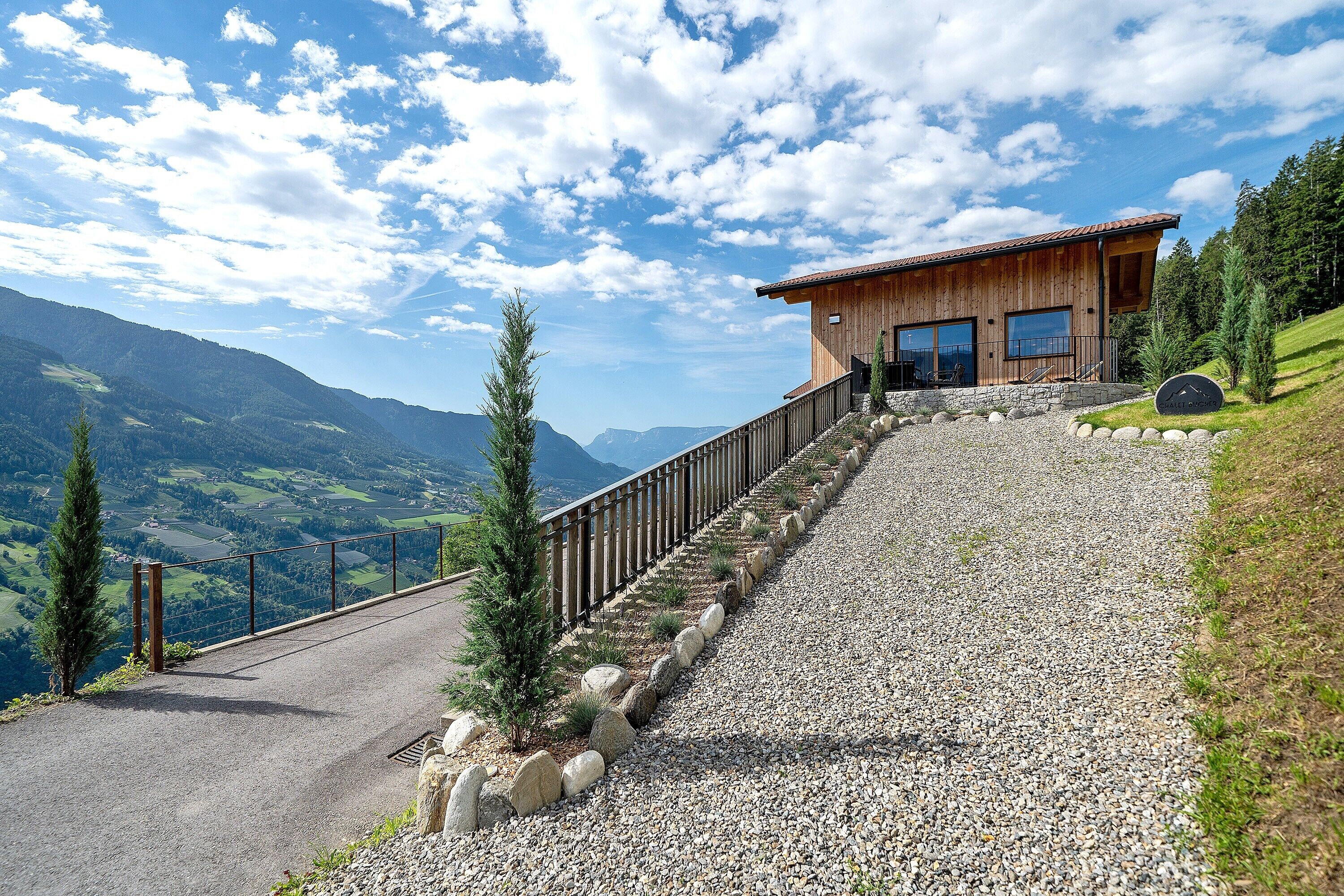 A wooden cabin with a gravel path leading to it, surrounded by mountains and clear skies.