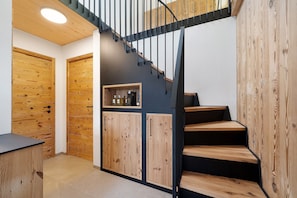 Una escalera con escalones de madera y barandilla negra, que conduce a una plataforma con estantería y armarios.