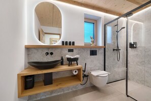 Une salle de bain moderne avec un meuble-lavabo en bois, un grand miroir, un évier, des toilettes et une douche séparée par une paroi de verre.