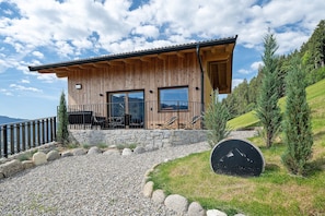 Una cabaña de madera con cimientos de piedra, ventanas amplias y un balcón con vistas a un paisaje montañoso.