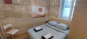 Une pièce avec un lit, une chaise, une fenêtre et un tableau au mur.