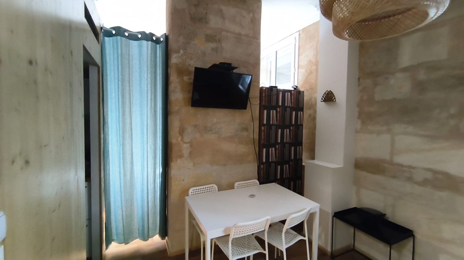 A room with a white table, chairs, a TV mounted on the wall, and a bookshelf.