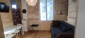 Une pièce avec un plancher en bois, une table blanche avec des chaises, une bibliothèque, un canapé, une horloge et une fenêtre donnant sur un beau paysage.
