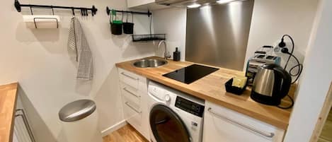 A compact kitchen with a washing machine, a sink, a stove, and a trash bin.