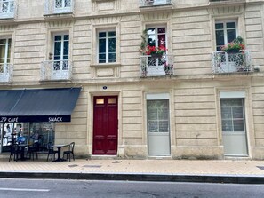Un bâtiment avec une porte rouge, de nombreuses fenêtres et des balcons ornés de jardinières.