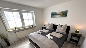 Un dormitorio con una cama grande, una ventana, un radiador y un cuadro en la pared.