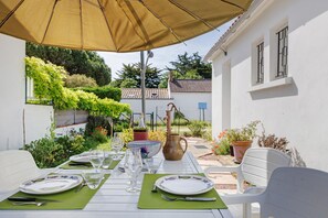 An outdoor dining area with a table set for four, surrounded by white chairs, under a large umbrella. - Spacious, Comfortable House in Barbâtre! (Barbâtre)