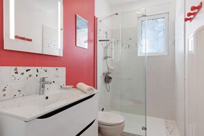 A bathroom with a white sink, a toilet, a glass shower enclosure, and a red accent wall. - Spacious, Comfortable House in Barbâtre! (Barbâtre)