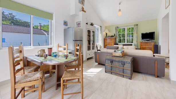 Un vaste espace de vie comprenant une table à manger, des chaises, un canapé, un téléviseur et une grande fenêtre donnant sur une maison.