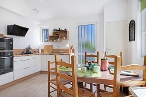 A modern kitchen with white cabinets, a Bosch oven, wooden chairs, and a dining table set for four. - Spacious, Comfortable House in Barbâtre! (Barbâtre)