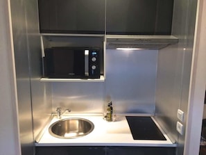 Eine kleine Küchenzeile mit Spülbecken aus Edelstahl, einer Mikrowelle und einem Einbauofen.