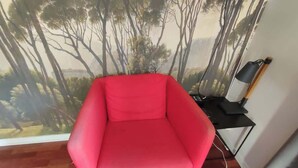 Een rode fauteuil in een kamer met een muurschildering van bomen.