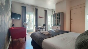 Een hotelkamer met een bed, een rode stoel, een bureau met stoel, een televisie en een raam met gordijnen.