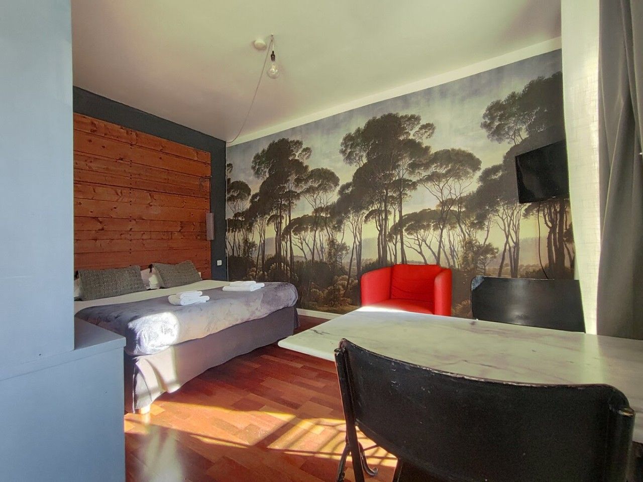 Une pièce comprenant un lit, une table à manger, une chaise rouge et une fresque représentant des arbres sur le mur.