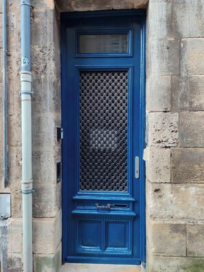 Eine blaue Tür mit einem Metallgitter, einem kleinen Fenster darüber und einem Klingelknopf.