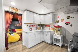 A compact kitchen with white cabinets, a yellow bean bag chair, and a popcorn machine. - The Boise Rec Retreat-theater, pool table, arcade (Boise)