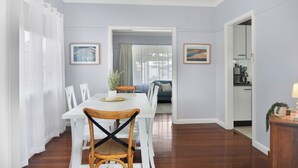Un comedor con una mesa blanca, sillas de madera y un ventilador de techo. Hay cuadros en las paredes y se ve una vista hacia otra habitación.