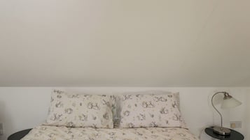 Una cama con estampado floral, una mesita de noche con lámpara y un enchufe en la pared.