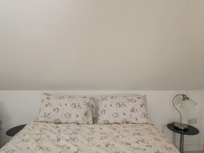 Un lit avec un motif floral, une table de chevet avec une lampe et une prise électrique au mur.