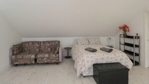 A bedroom with a bed, a sofa, a small round table, and a shelf with a vase of flowers. - The Nest (Glastonbury)