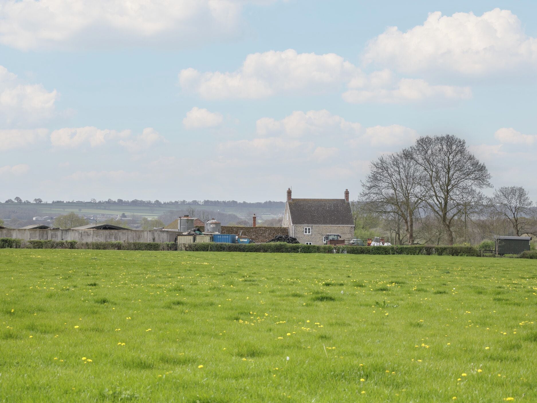 Ländliche Landschaft mit einem Haus, offenen Feldern und fernen Hügeln.
