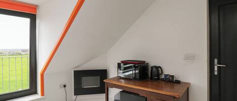 Ein Zimmer mit schräg stehender Decke, einem Schreibtisch mit Wasserkocher, Mikrowelle und kleinem Kühlschrank.