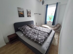 Un dormitorio moderno con una cama, una mesita de noche, una lámpara y dos cuadros colgados en la pared.