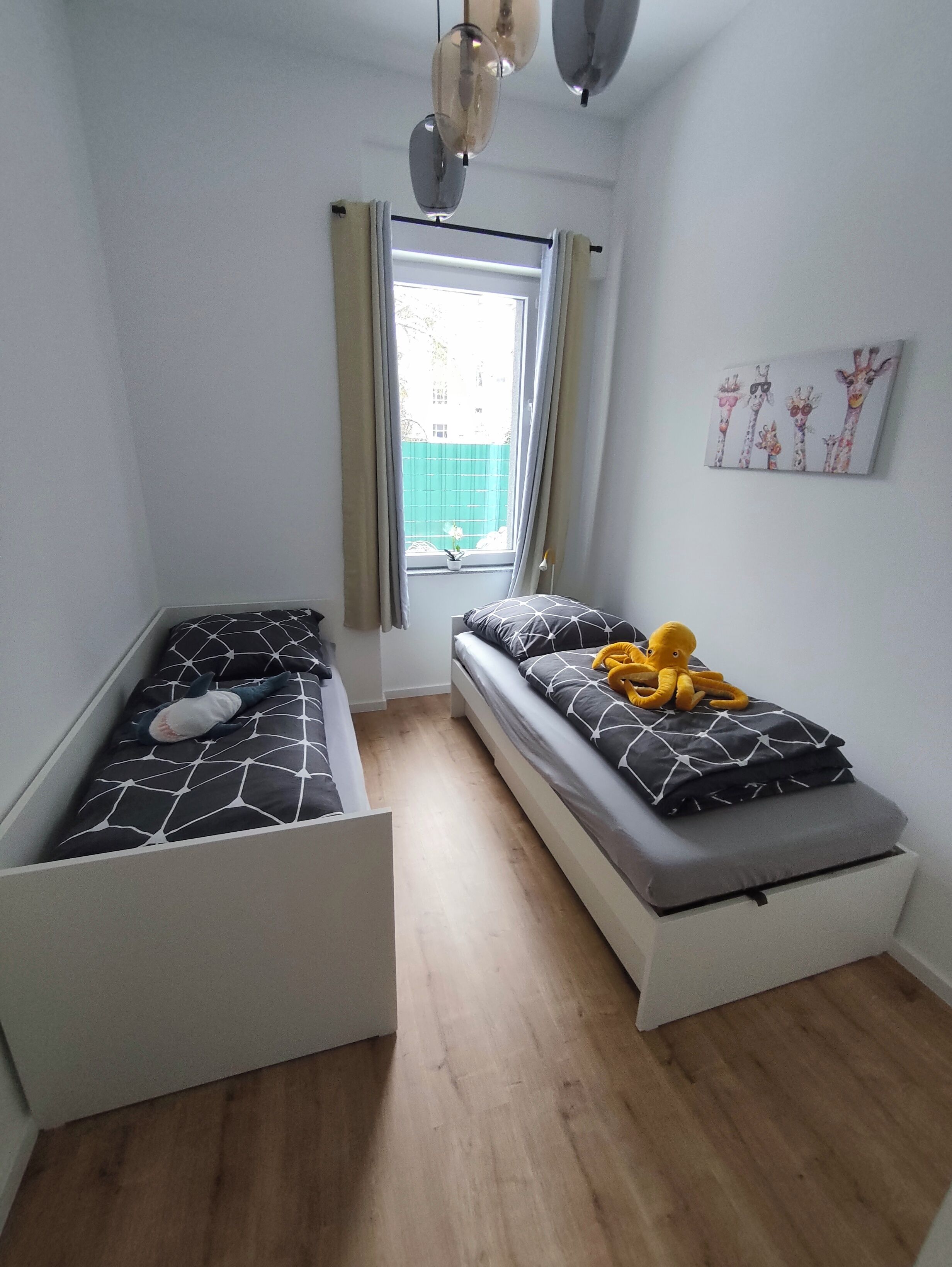 Ein gemütlicher Raum mit zwei Betten, einem Vorhangfenster, einer Deckenleuchte und einem Wandbild.