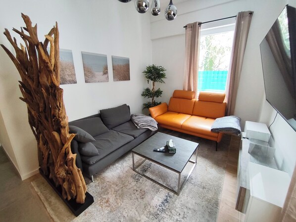 Una sala de estar con un sofá gris, un sofá naranja, una mesa de centro, una escultura de madera y un televisor.