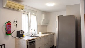 Cuina compacta amb rentaplats integrat, nevera d'acer inoxidable i finestra amb cortines.