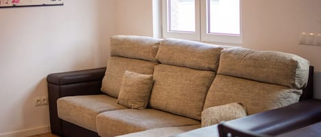 Un sofá con varios cojines, suelo de madera y una ventana con persianas.