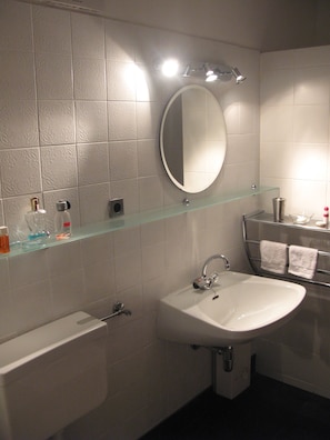 A bathroom with a white sink, a glass shelf, a mirror, and a toilet.