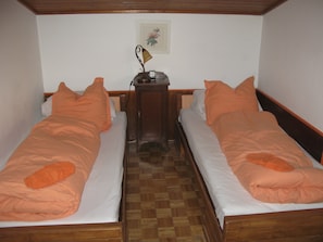 A room with two single beds, a wooden headboard, a small wooden nightstand with a lamp, and a framed picture on the wall.