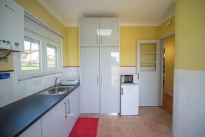 Een keuken met witte kasten, een magnetron en een rood vloerkleed.