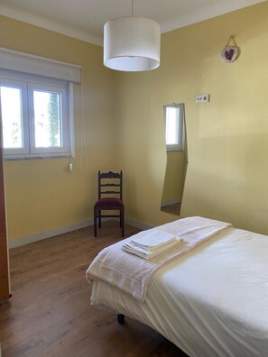 Een slaapkamer met een bed, een stoel, een raam en een spiegel.