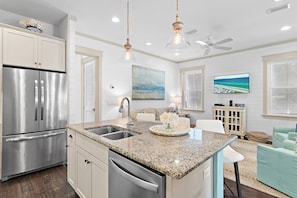 A kitchen with a stainless steel refrigerator, granite countertops, and a ceiling fan. - Sandgrass Sanctuary | 30A | Golf Cart, Bikes | Sleeps 11 (Santa Rosa Beach)