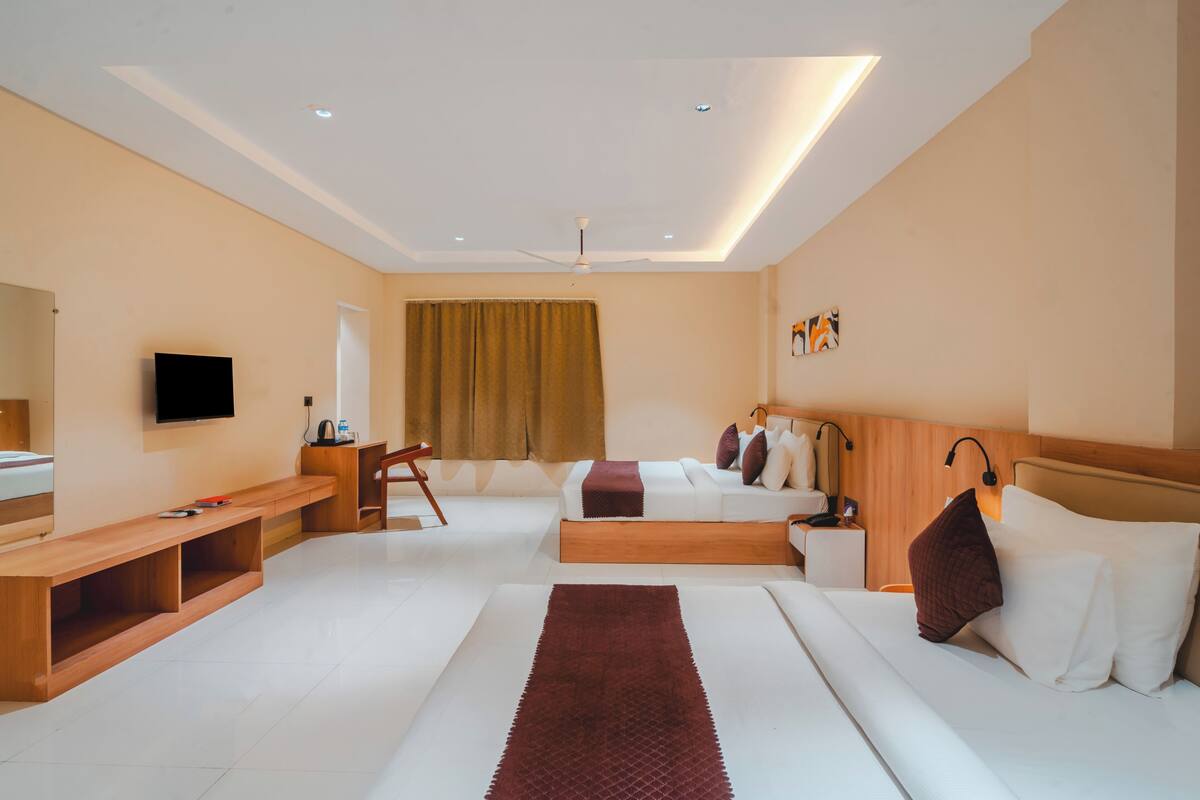 A modern hotel room with a large bed, a smaller bed, a desk, a chair, a TV, and a window with curtains.
