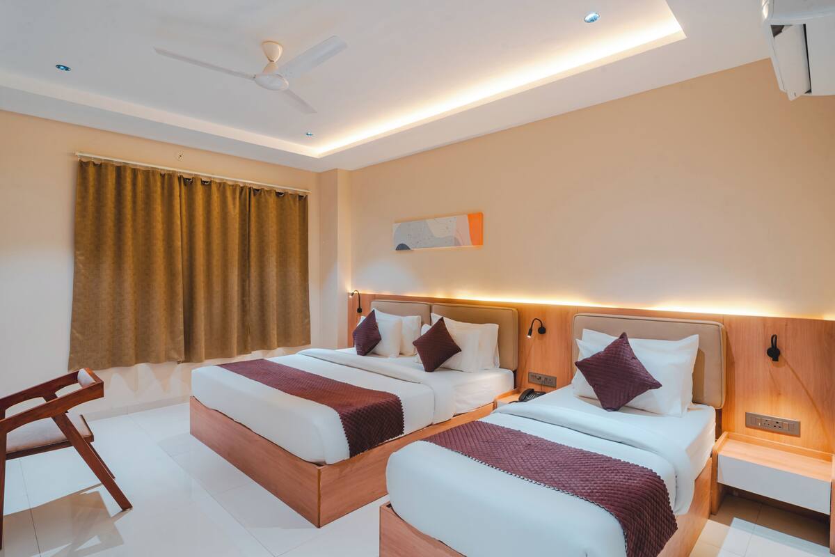 A hotel room with two beds, a desk, a chair, and a ceiling fan.