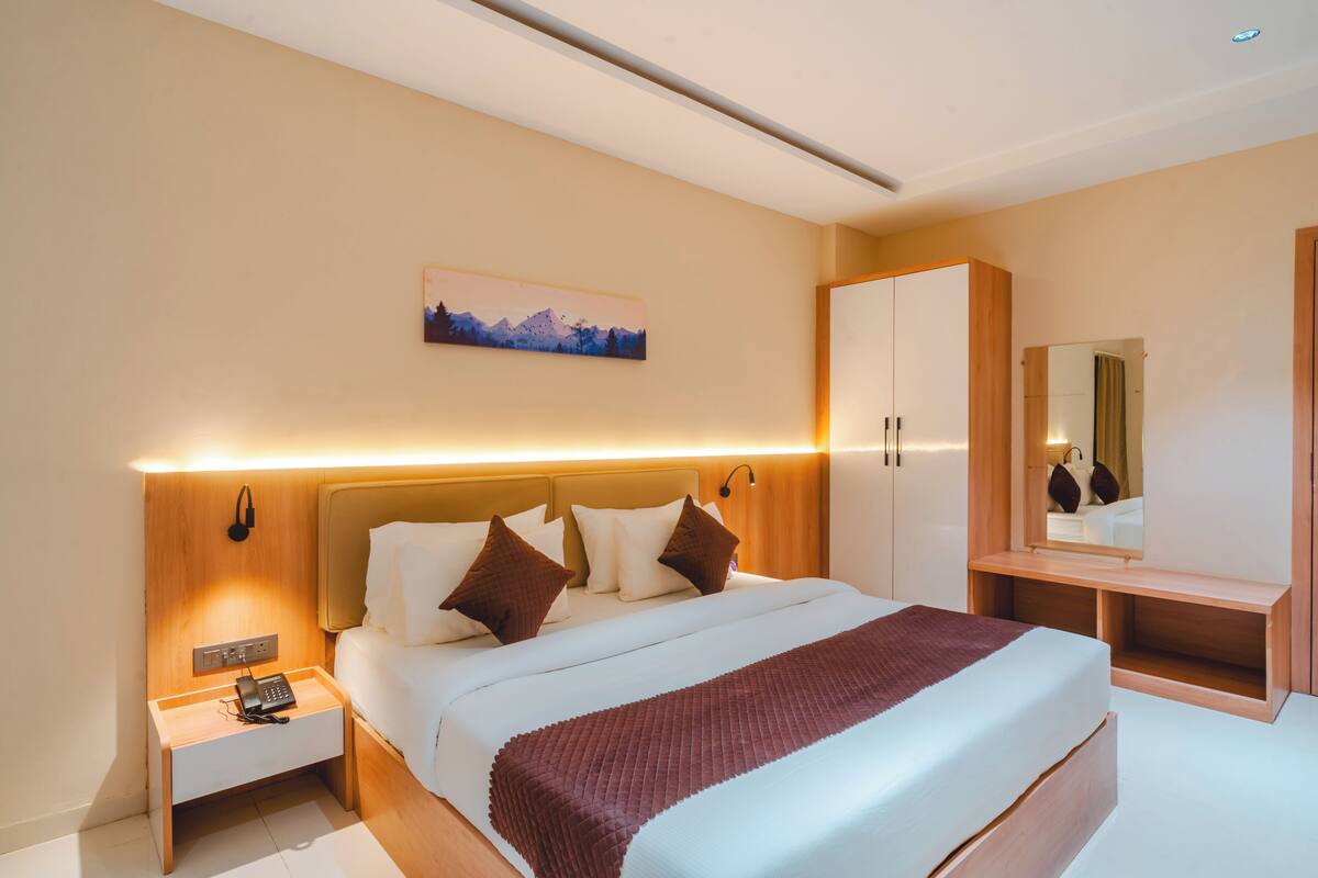 A hotel room with a bed, bedside table, nightstand, and a mirror.