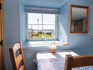 A bedroom with a window view of a landscape, a bedside table with a lamp, and a mirror on the wall.
