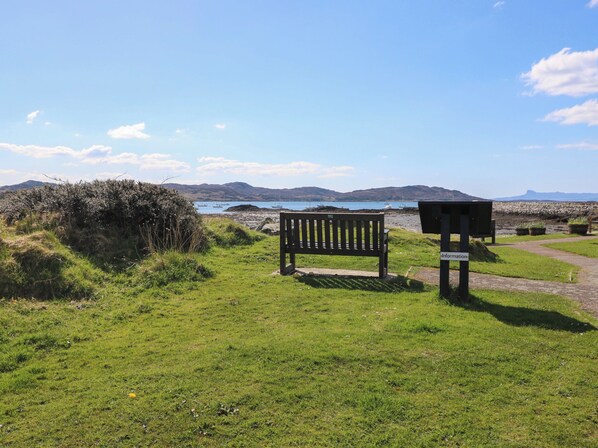A grassy area with a wooden bench and a signpost. - Post Cottage (Arisaig)