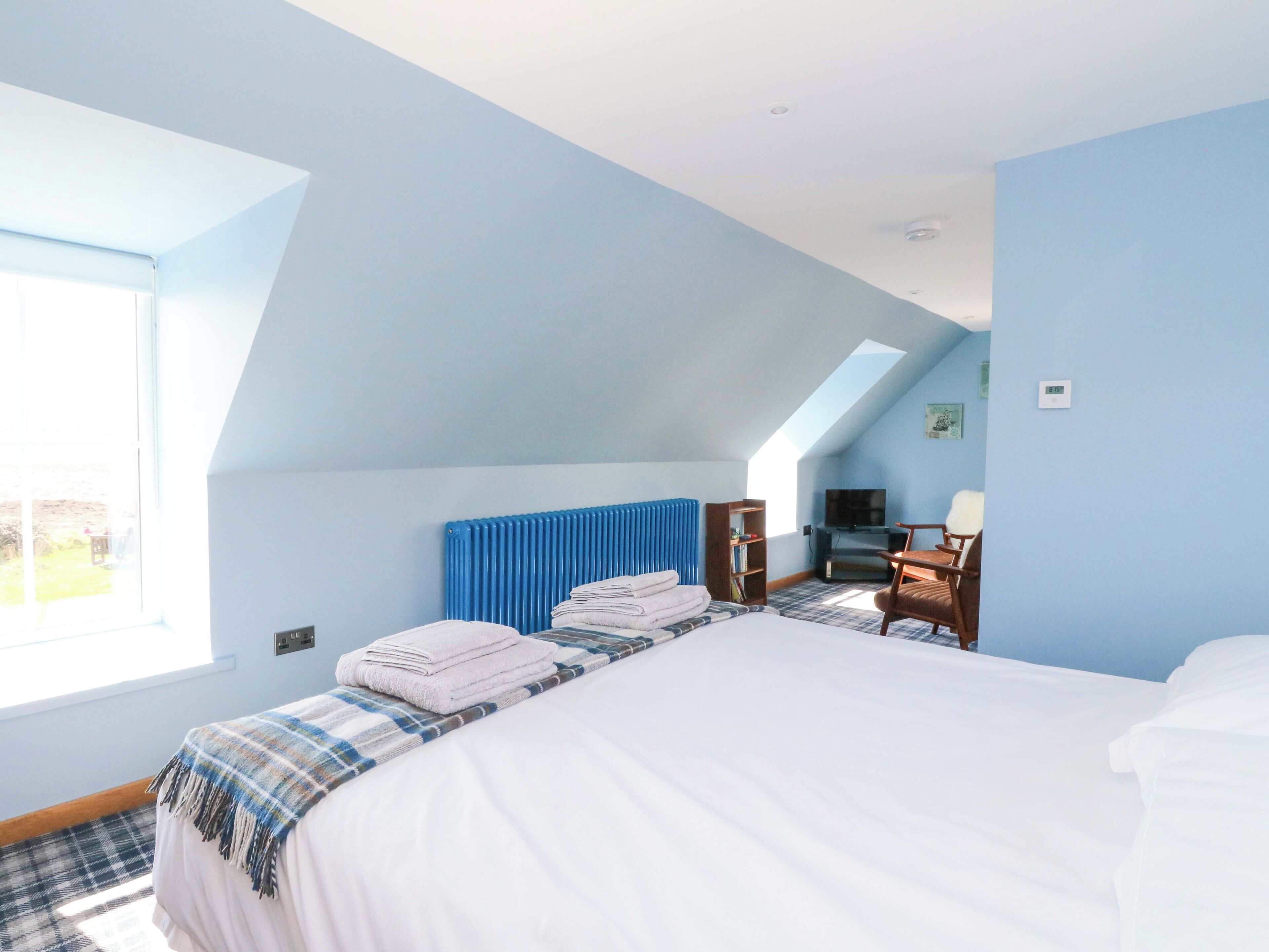 A bedroom with a bed, a radiator, a TV, and a window.