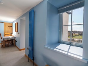 A room with a window, a radiator, a wooden door, and a table with chairs. - Post Cottage (Arisaig)