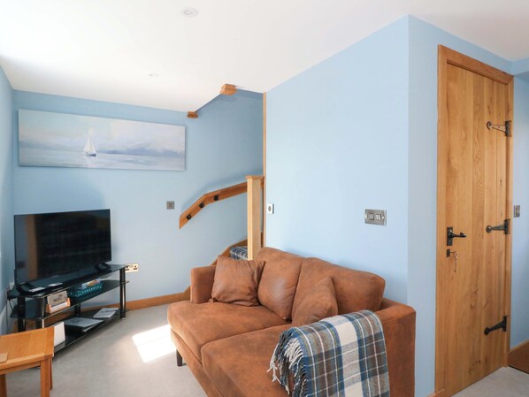 A living room with a brown sofa, a television on a stand, a wooden door, and a painting on the wall.
