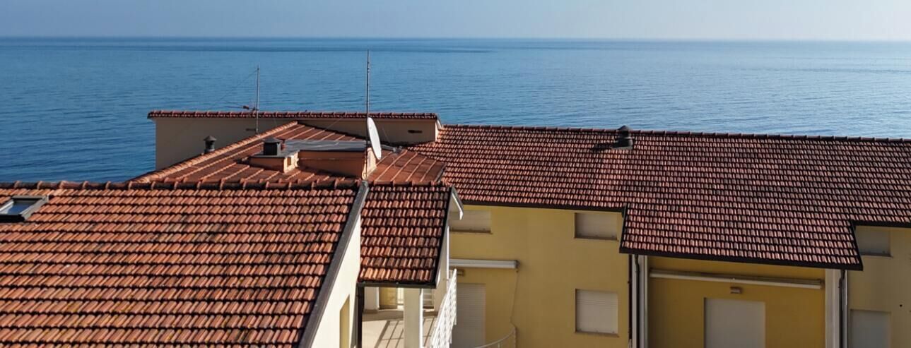 Un bâtiment situé sur la côte, avec des toits recouverts de tuiles en terre cuite et une vue sur la mer.